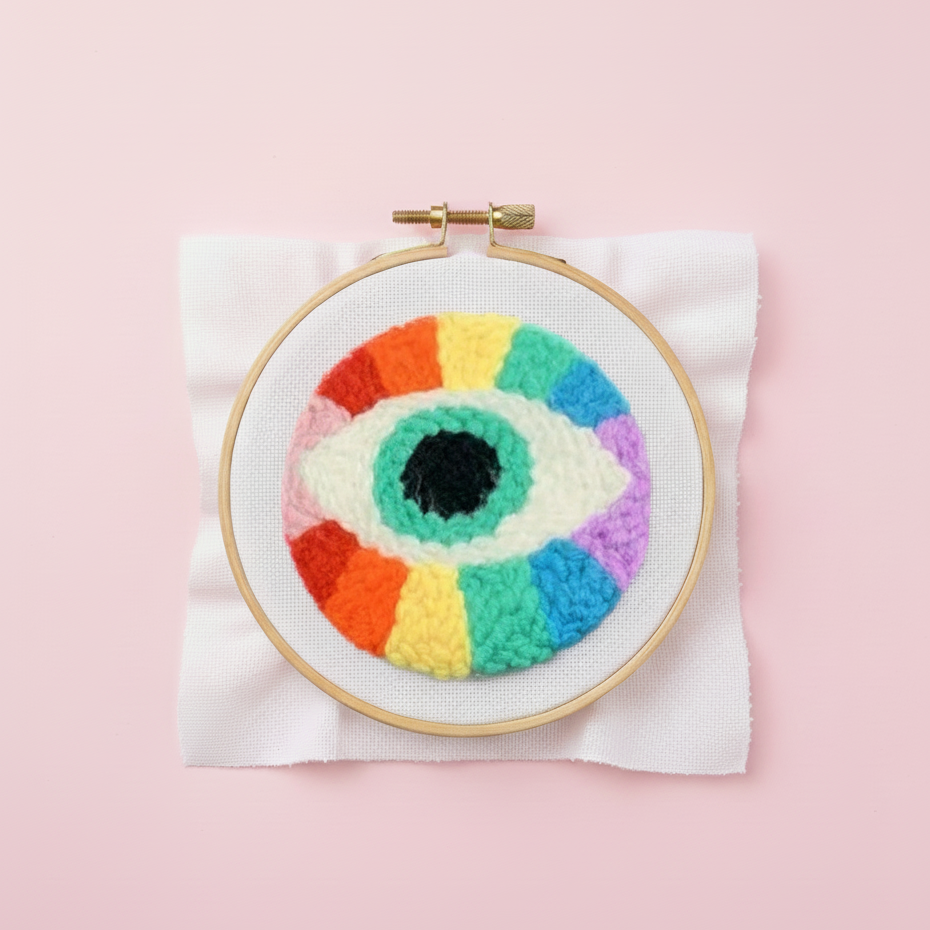 Embroidery hoop with colorful eye design on a pink background
